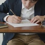 collégien assis à un bureau écrivant une lettre