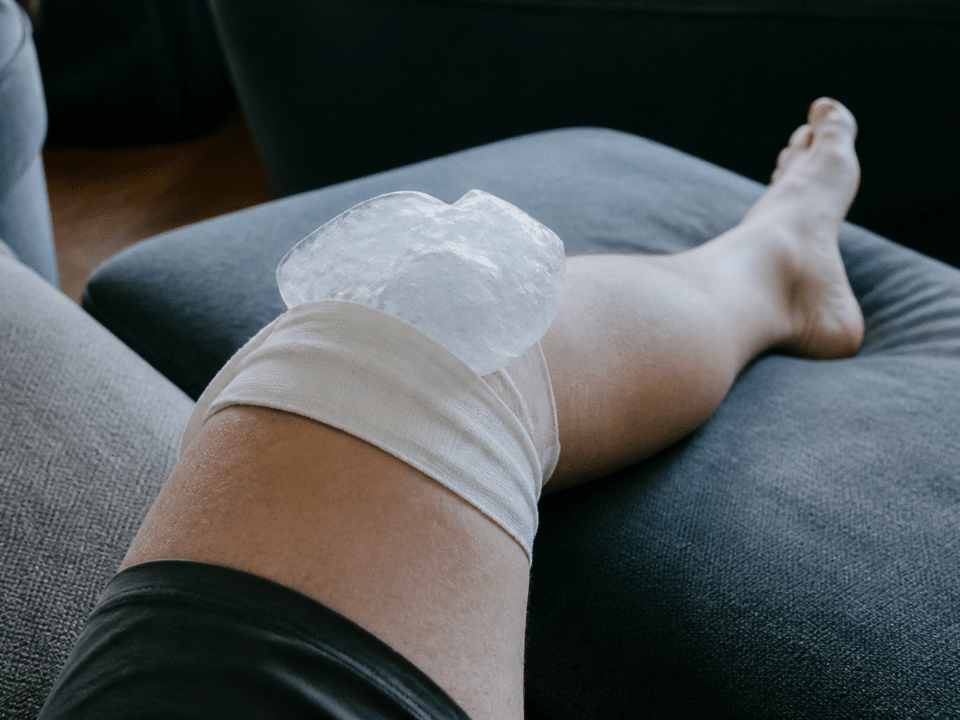 Genou enflé avec glaçon posé dessus, immobilisé.