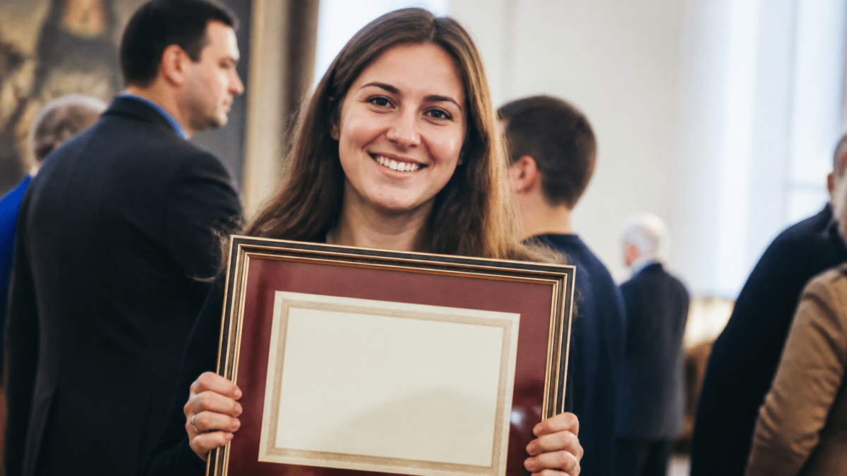 Personne souriante tenant un parchemin diplôme encadré