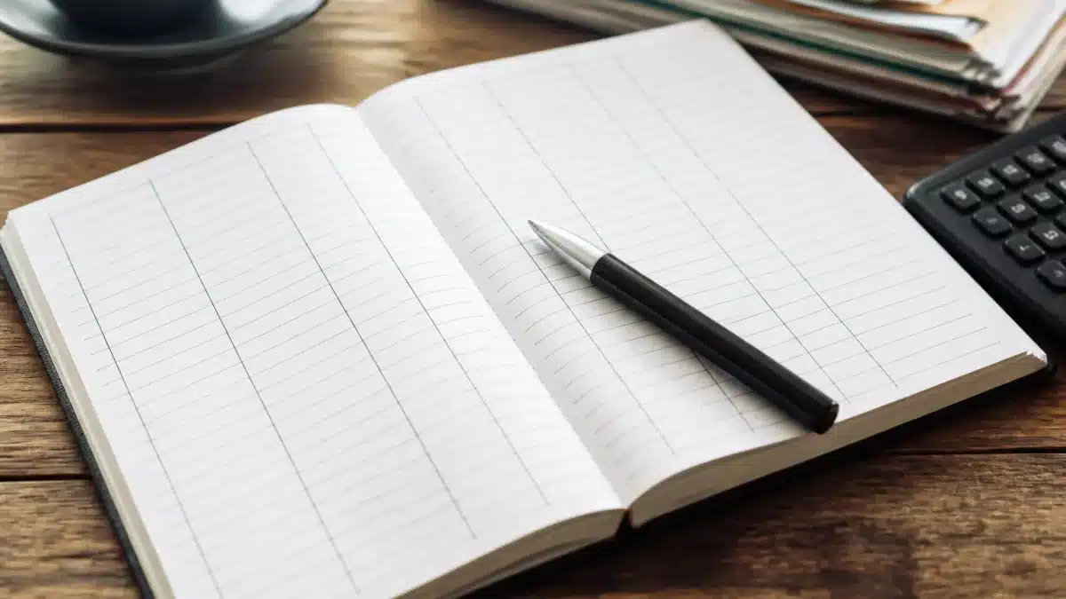 Carnet ouvert affichant colonnes depenses avec stylo pose dessus