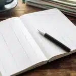 Carnet ouvert affichant colonnes depenses avec stylo pose dessus