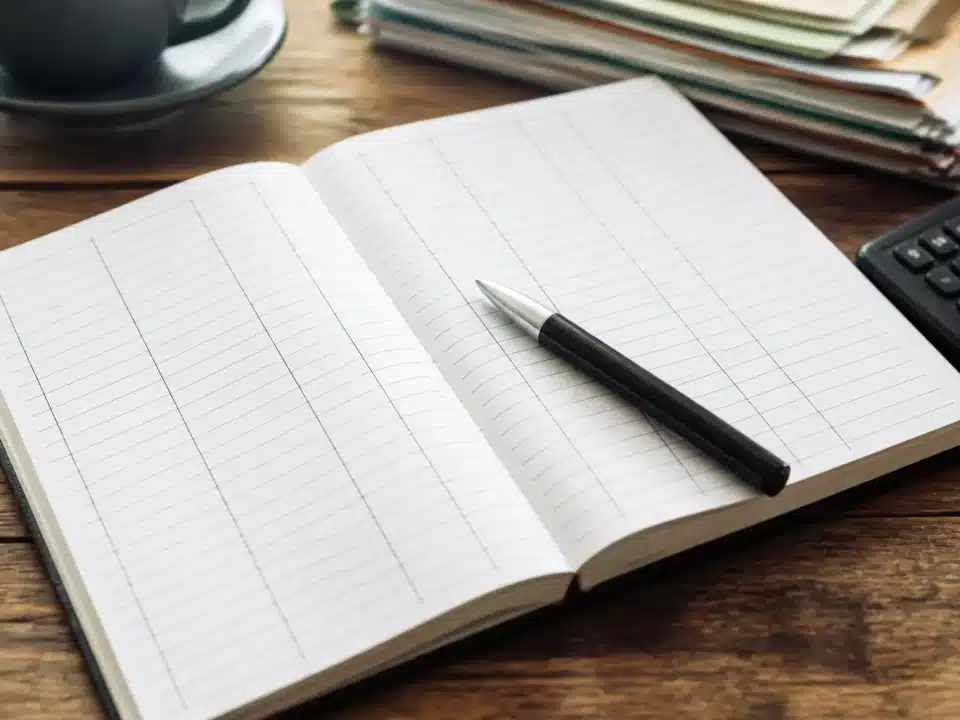 Carnet ouvert affichant colonnes depenses avec stylo pose dessus