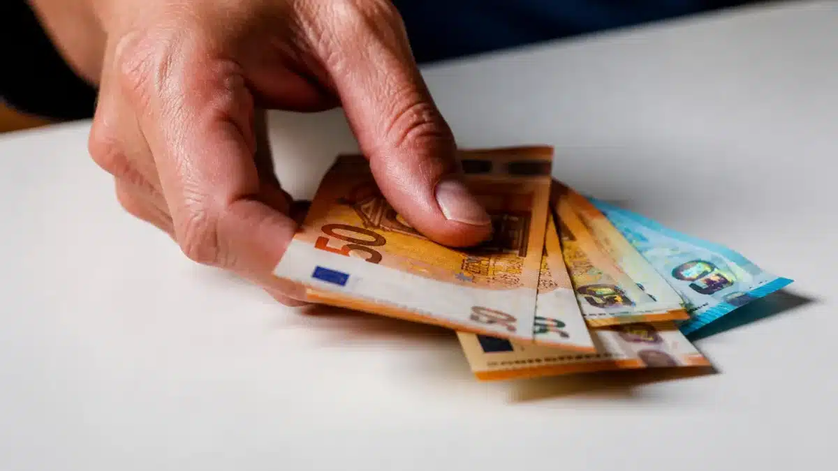 Main posant plusieurs billets d'euros sur table blanche