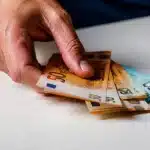 Main posant plusieurs billets d'euros sur table blanche